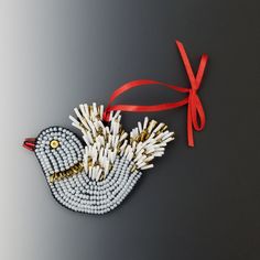 an ornament made out of matches and beads with a red ribbon hanging from it