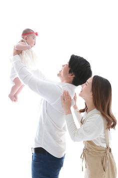 a man holding a baby up to his face while two women hold him in the air