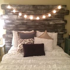 a bed that has some lights on the headboard and pillows in front of it