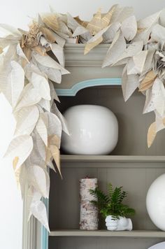 a book shelf with some white vases on top of it and plants in the middle