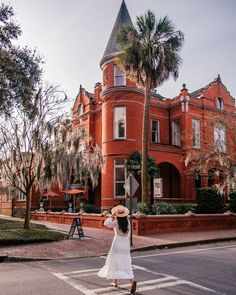 a woman crossing the street in front of an old red brick building with a tower