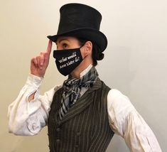 a woman wearing a top hat and vest with a black face mask on her face