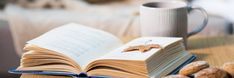 an open book sitting on top of a table next to nuts and a coffee cup