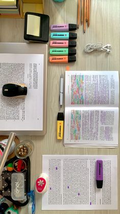 several books, pens and markers are on the table next to each other with writing utensils