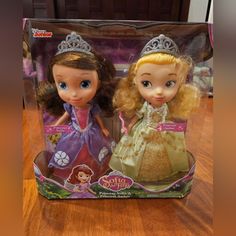 the two dolls are in their boxes on the table, one is wearing a tiara