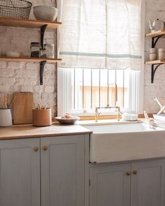 a white kitchen sink sitting under a window next to a wooden shelf filled with pots and pans