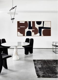 a dining room with black chairs and a white table in the center, an abstract painting on the wall