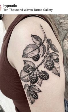 a woman's shoulder with black and white tattoos on her arm, holding a branch