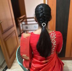 a woman with long black hair sitting in a chair wearing a red sari and braid