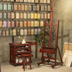 an easel and two chairs in front of a wall full of jars on shelves