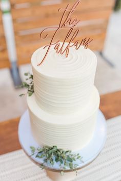 a white wedding cake sitting on top of a table next to a wooden sign that says the falls