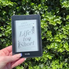 a person holding up a kindle book in front of green bushes and shrubbery