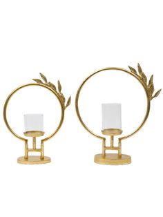 two gold candle holders with white glass on each one and an olive branch design at the top