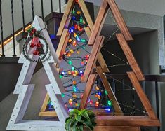 three wooden christmas trees with lights on them sitting in front of a banister and stairs