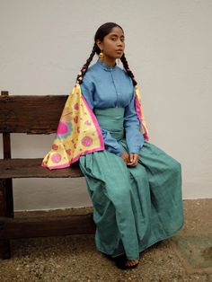 a woman sitting on a wooden bench wearing a blue shirt and green skirt with pink polka dots