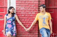 a man and woman holding hands in front of a brick wall with writing on it