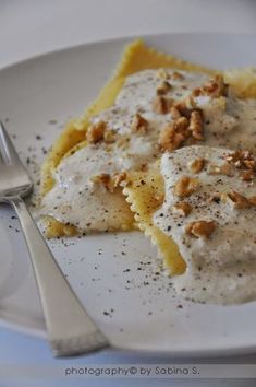 a white plate topped with ravioli covered in sauce and walnuts next to a fork