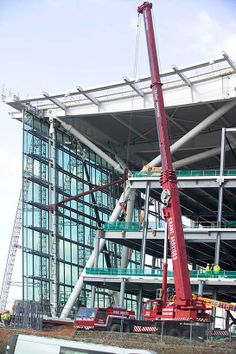 a large crane is in front of a building with glass walls and steel bars on the sides