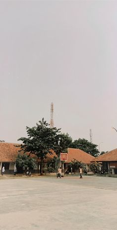 two people playing basketball in an empty parking lot next to some trees and buildings with radio towers on the roof