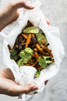 a person holding a paper bag filled with fries and guacamole wedges