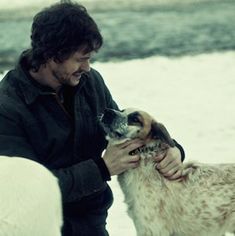 a man petting a dog on the nose while standing next to snow covered ground