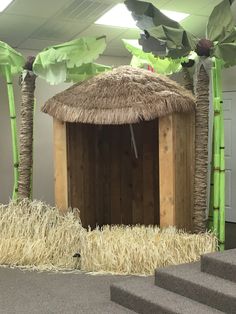 an outhouse with grass and palm trees on the outside, surrounded by straw bales