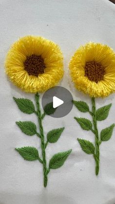 two sunflowers are on a white piece of cloth with green leaves and brown center