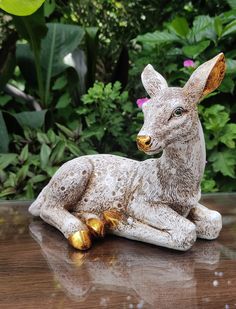 a statue of a deer laying on top of a wooden table next to some plants