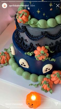 a three tiered cake with pumpkins and ghost faces on the side, sitting next to an orange candle