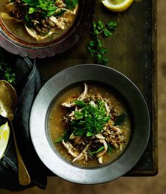 two bowls filled with soup and garnished with parsley, lemon wedges and cilantro