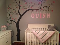 a baby's room decorated in pink and gray with a tree painted on the wall