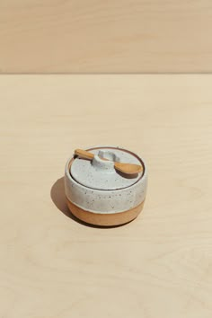 a white ceramic container with a wooden spoon in it on top of a wood table