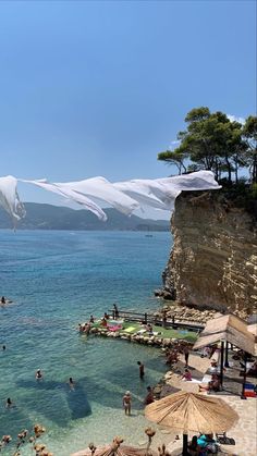 people are swimming in the blue water near some cliffs and mountains with snow on them