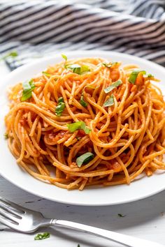 a white plate topped with spaghetti and garnished with parsley next to a fork