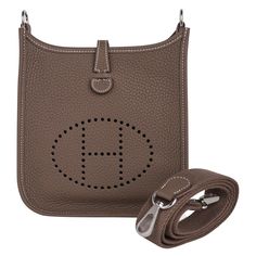 Mightychic offers an Hermes Evelyne TPM bag featured in neutral Etoupe. Plush clemence leather and matching Etoupe canvas sport strap. Signature perforated H on front of bag. Fresh with palladium hardware. Fabulous shoulder or crossbody bag. Sport strap in textile with leather and palladium hardware details. Comes with sleepers and signature Hermes box. NEW or NEVER WORN The Hermes mini bag price maintains its value due to the high demand of this rare style. Mightychic - your Hermes online boutique for a superior shopping experience. Private and Confidential consignment services offered final sale BAG MEASURES: LENGTH 6.5" TALL 7.5" DEEP 2" STRAP DROP 21" CONDITION: NEW or NEVER WORN Hermes Mini Bag, Hermes Evelyne Tpm, Hermes Crossbody Bag, Hermes Evelyn Bag, Designer School Bags, Sport Armband, Hermes Box, Boutique Online, Hermes Bags