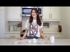 a woman standing in front of some jars on a kitchen counter with an oven and microwave behind her