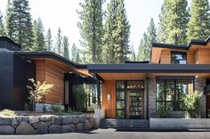 a modern house in the woods with large windows and stone walls on both sides, surrounded by pine trees