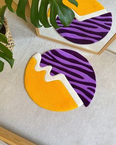 two circular rugs with purple, yellow and white designs on them next to a potted plant