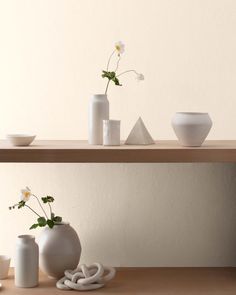 three white vases with flowers in them sitting on a shelf next to other items