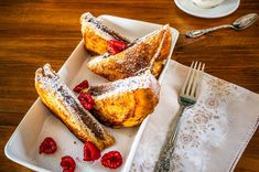 powdered sugar covered pastries on a white plate with raspberries and silverware