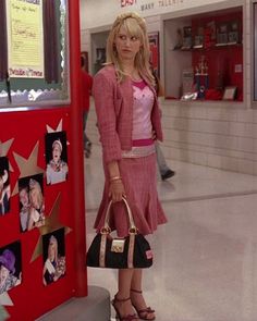 a woman standing next to a red wall holding a purse and looking at the camera