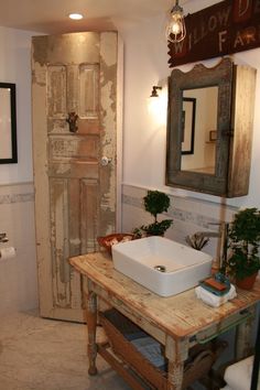 a bathroom with a sink, mirror and potted plants on the counter top in front of an old door