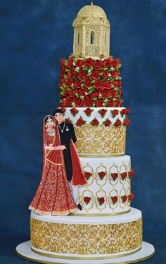 a wedding cake decorated with red roses and gold trimmings on a blue background