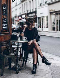 a woman sitting at a table with her legs crossed and drinking from a coffee cup