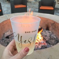 a person holding up a glass with the word yes on it in front of a fire pit