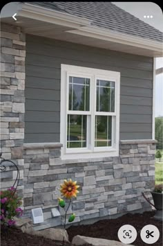 a sunflower sitting in front of a window on the side of a gray house