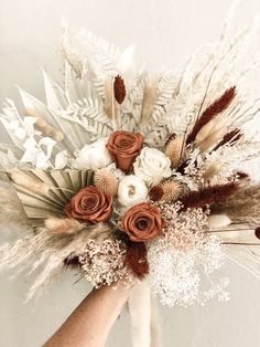 a hand holding a bouquet with flowers and feathers