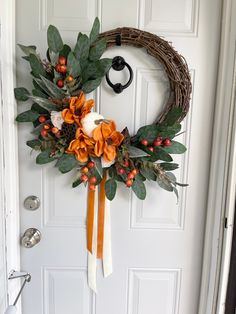 a wreath with orange flowers and greenery hangs on the front door