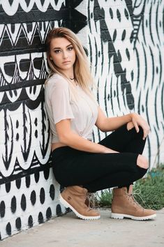 a beautiful young woman sitting on the ground next to a wall with black and white designs