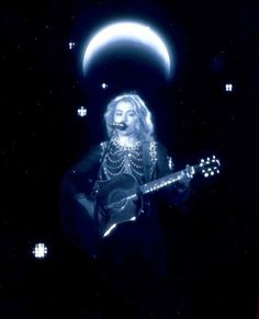 a woman holding a guitar standing in front of the moon with her face covered by chains